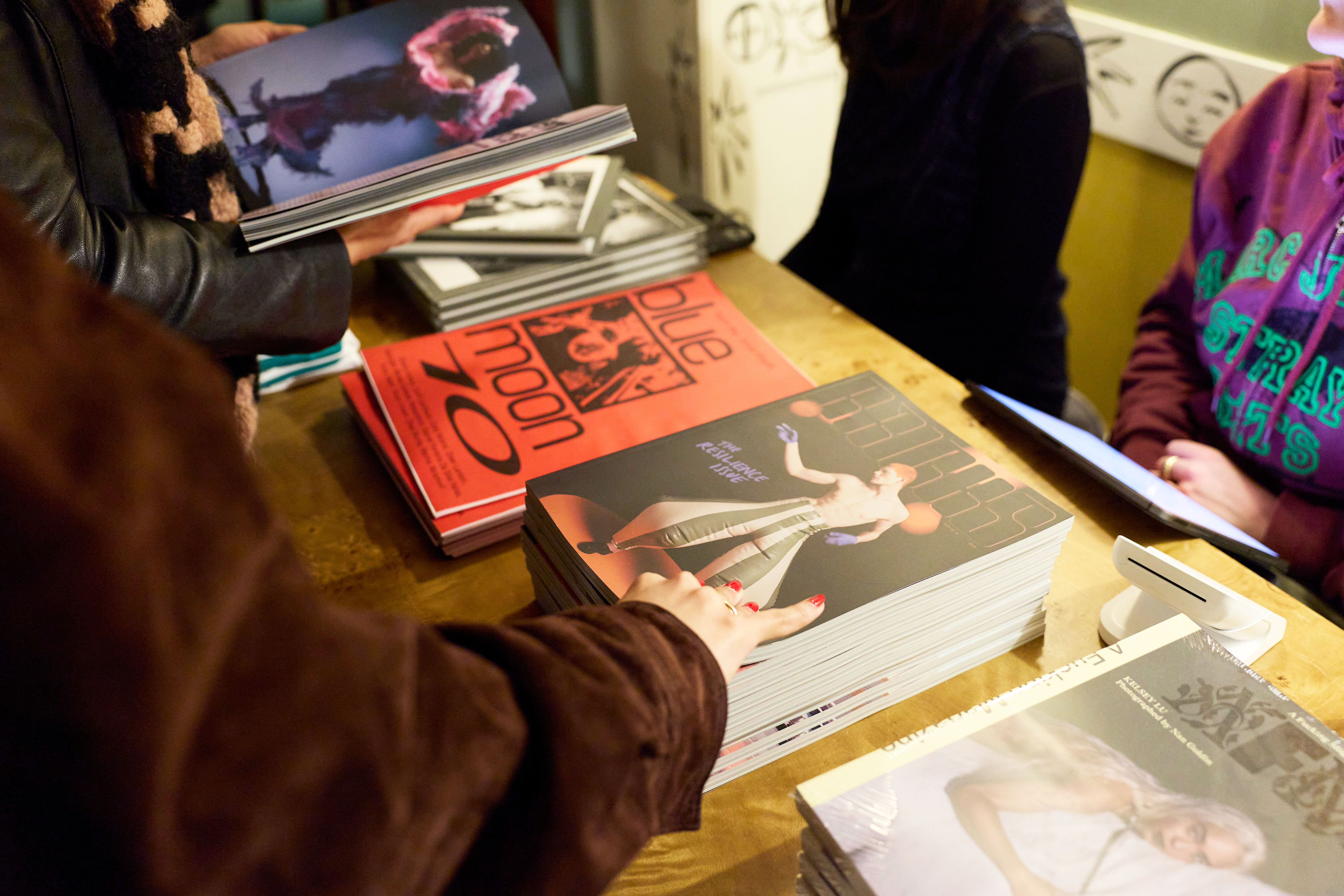 Stacks of independent art and photography books on a wooden table at a book fair.