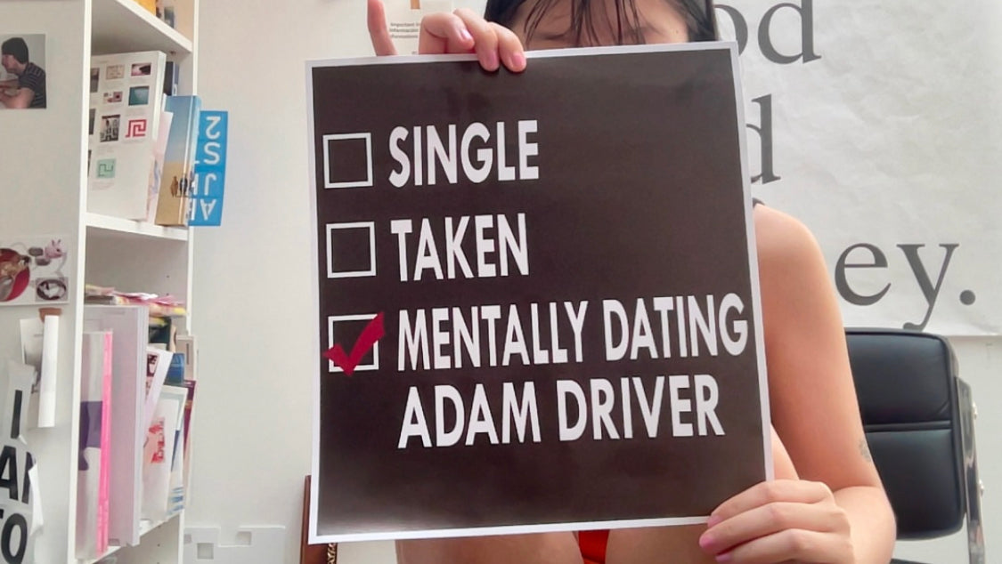 Person holding a sign that says 'MENTALLY DATING ADAM DRIVER' with a checkmark.