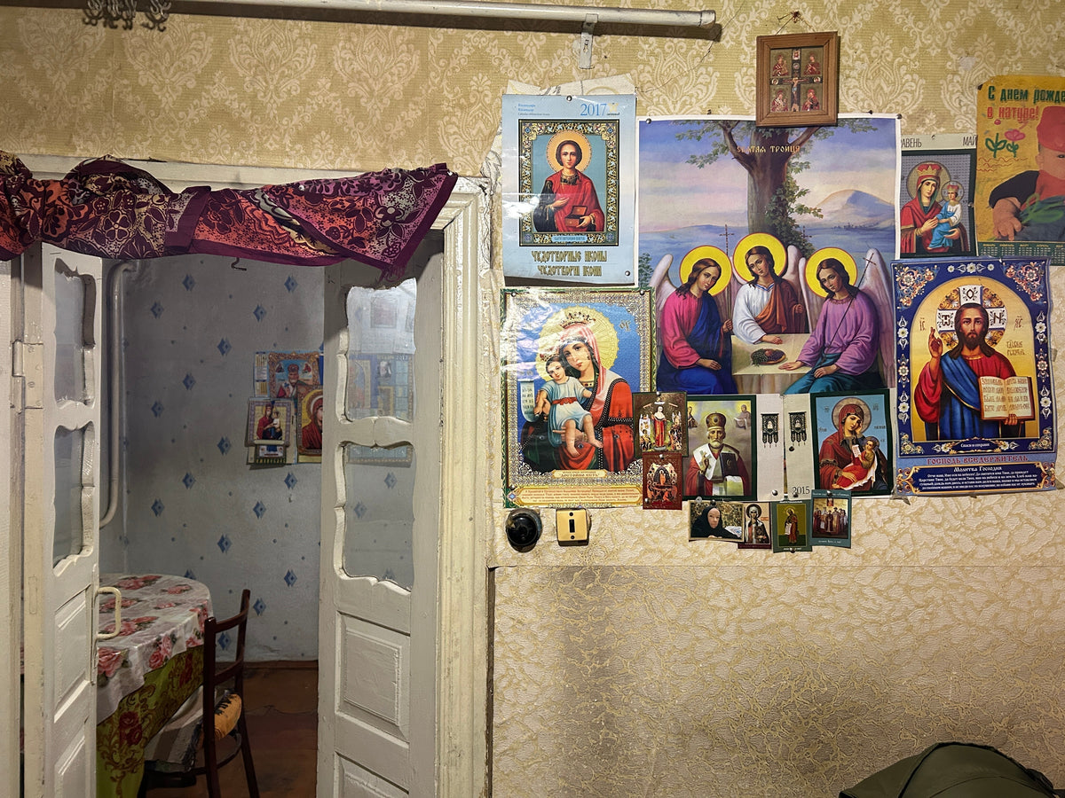 Various Orthodox Christian icons and posters displayed on a textured wallpaper wall next to a doorway.