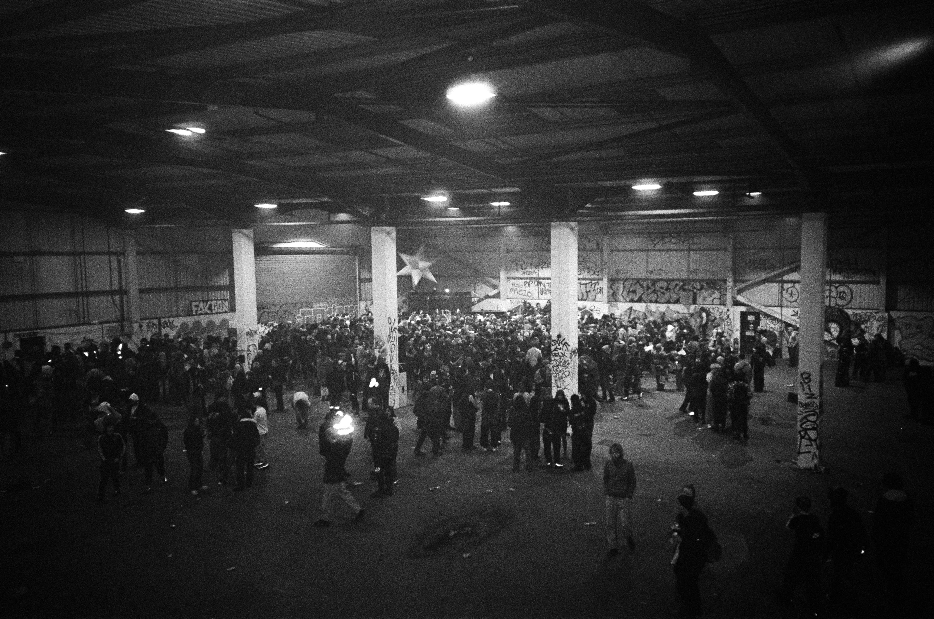 Black and white photo of a crowd in a large warehouse with graffiti on the walls.