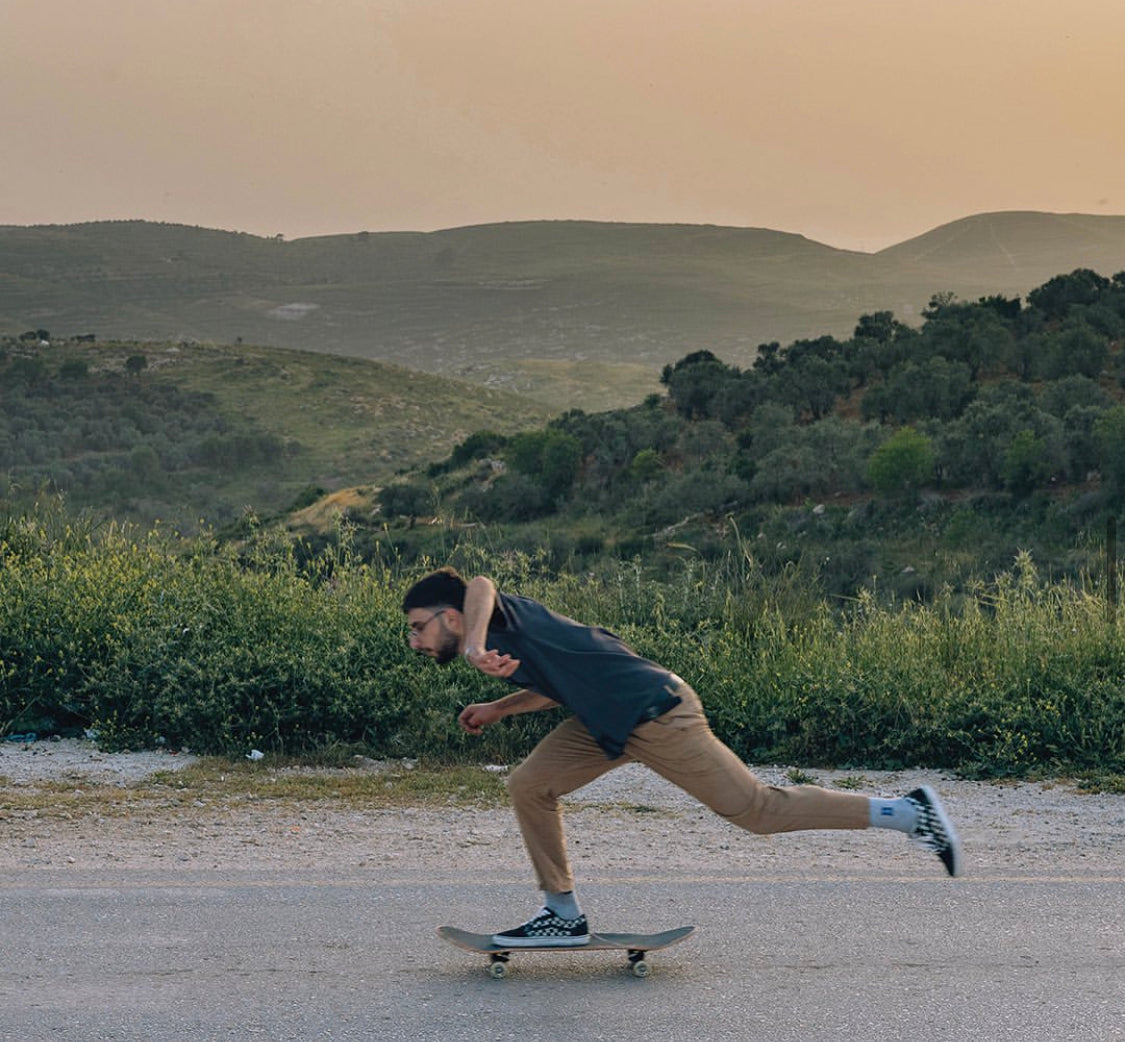 A man skateboarding on a paved road with rolling green hills in the background.