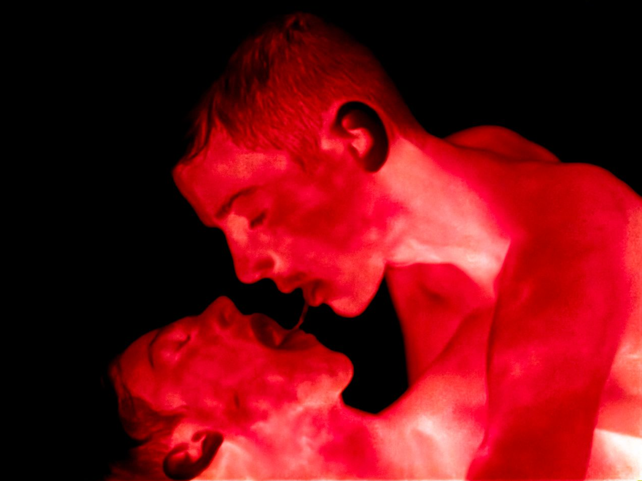 Two people in a close, intimate embrace bathed in saturated red light.