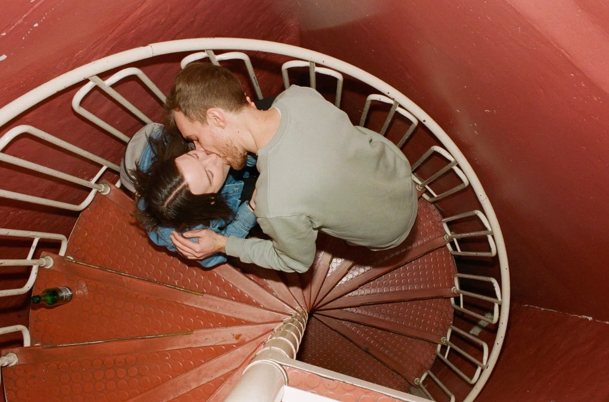 A man and woman kissing on a red spiral staircase.
