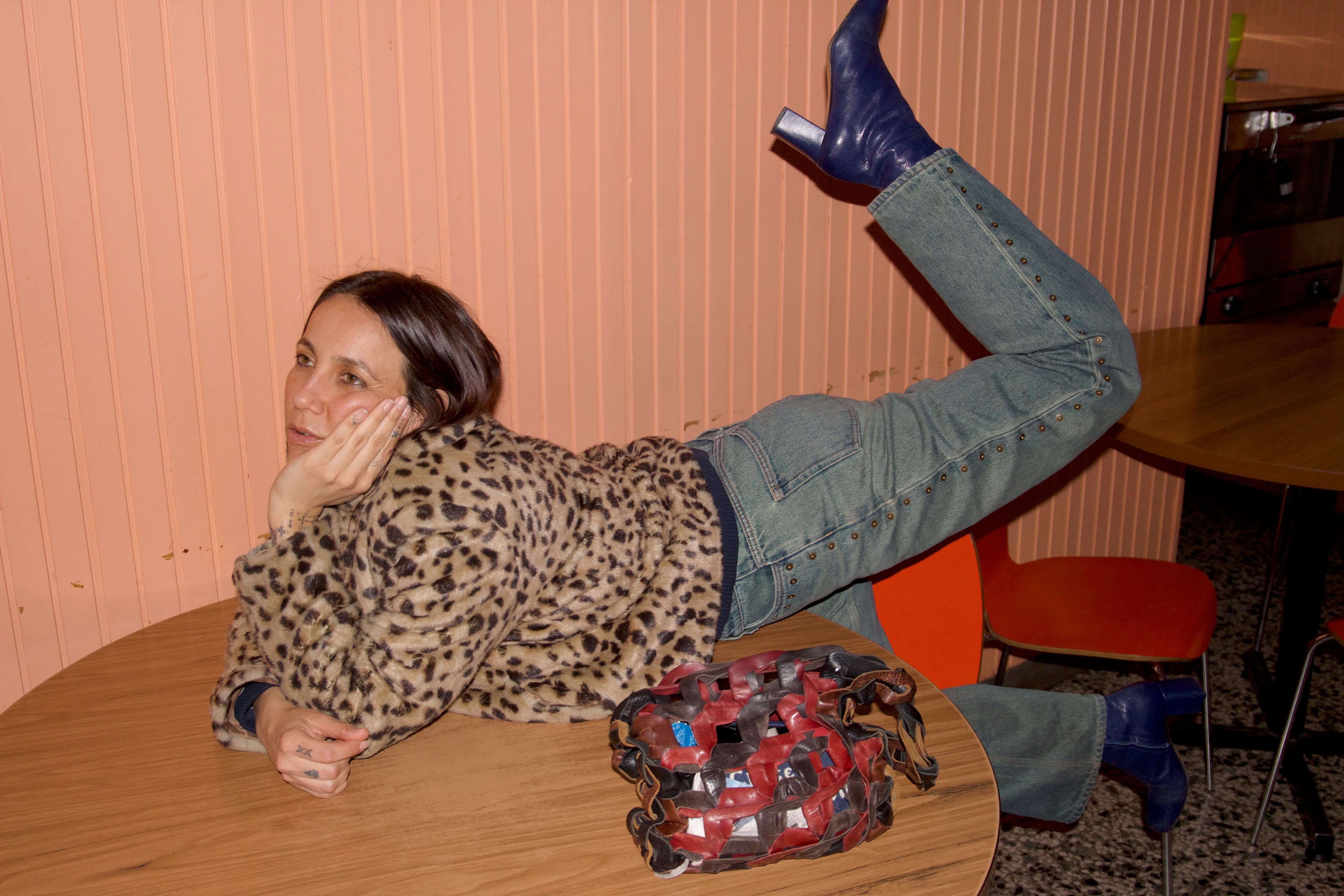 Woman in leopard print top and studded jeans reclining on a wooden table.