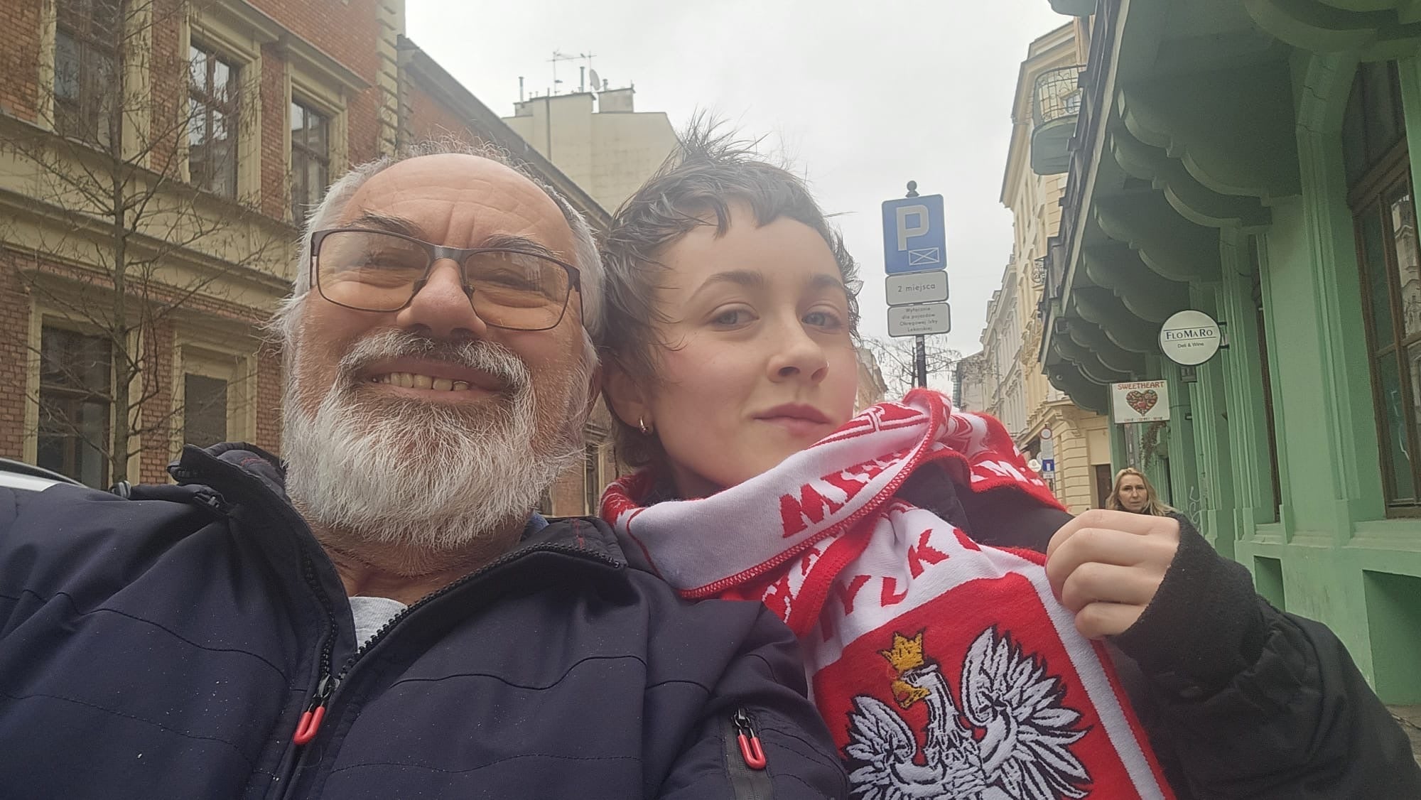 A selfie of an older man with a beard and a younger woman wearing a red and white Polish scarf.