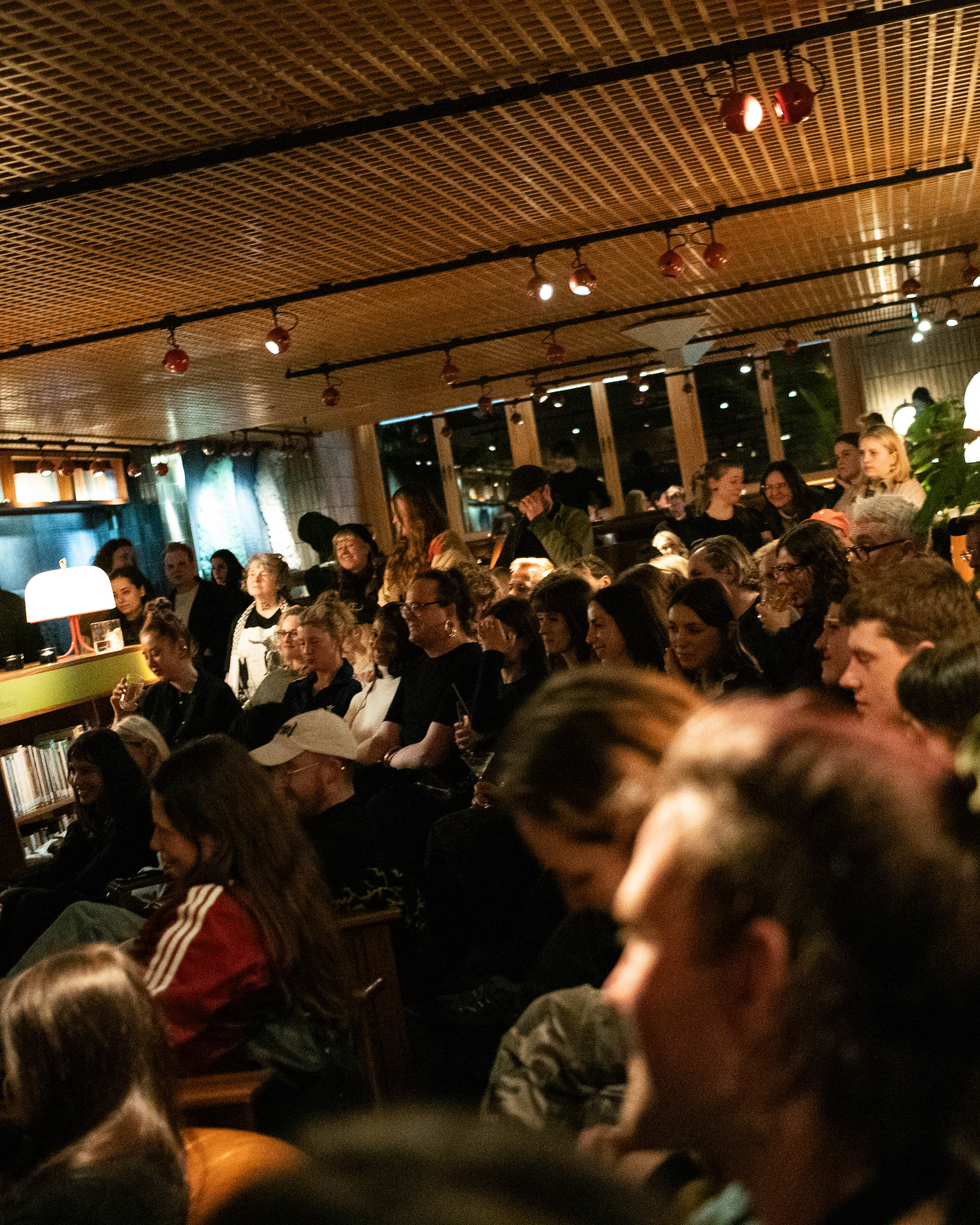 A crowded indoor event with a diverse group of people gathering in a dimly lit space.