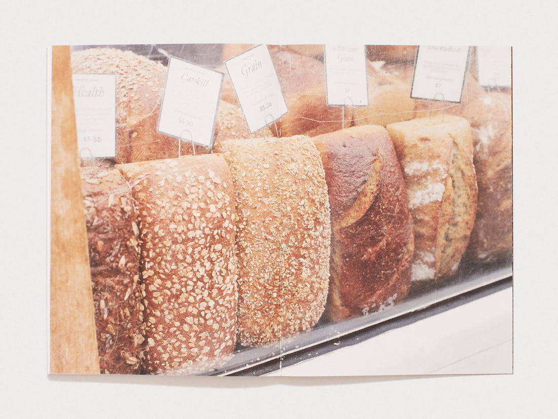 A row of various artisanal loaves of bread with price tags in a bakery display.