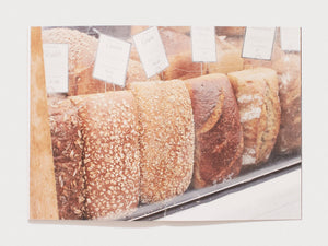 A row of various artisanal loaves of bread with price tags in a bakery display.