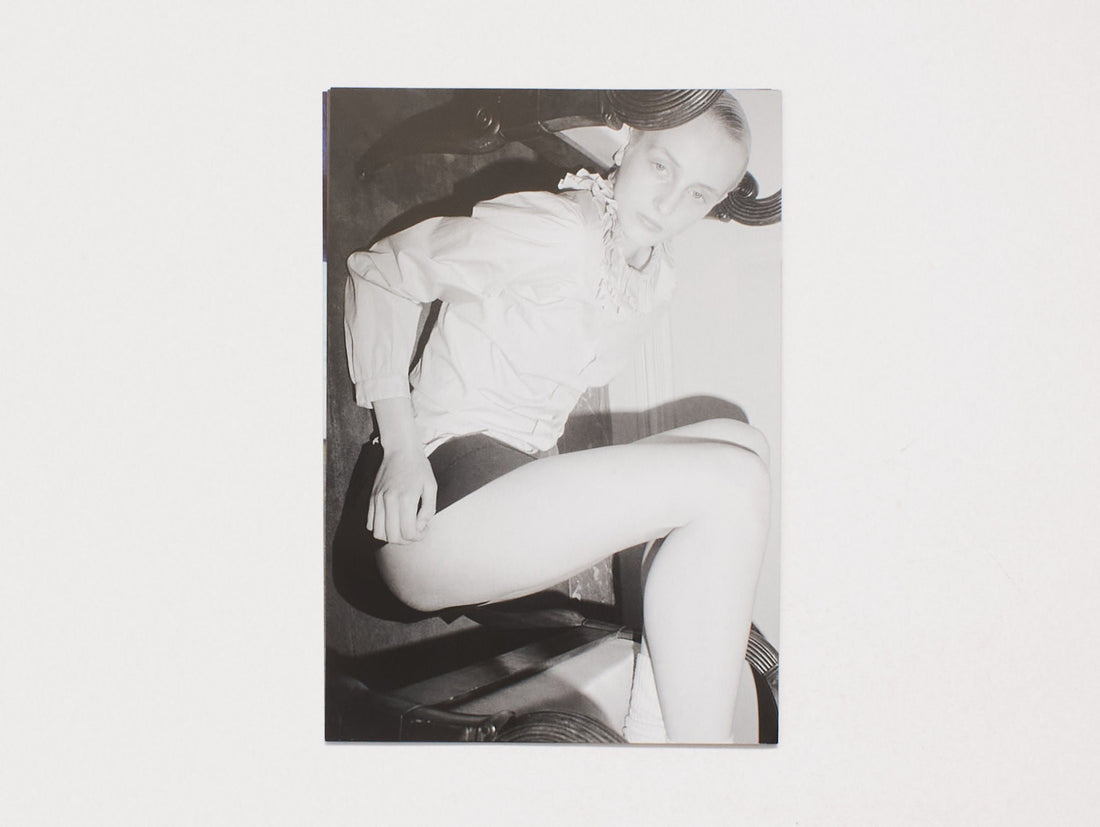 Black and white photograph of a person wearing a white blouse and dark shorts, posing in a chair.