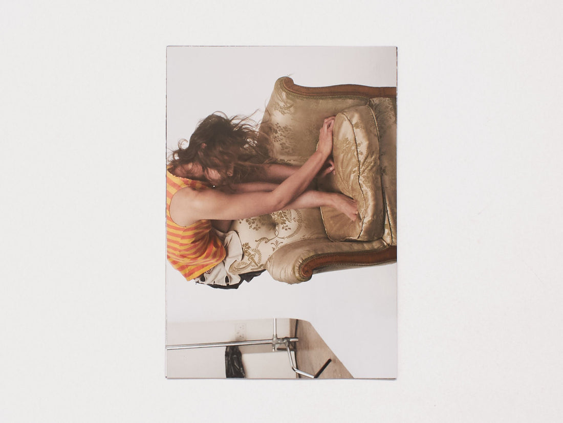 A person in a striped shirt curling up on a vintage beige armchair.