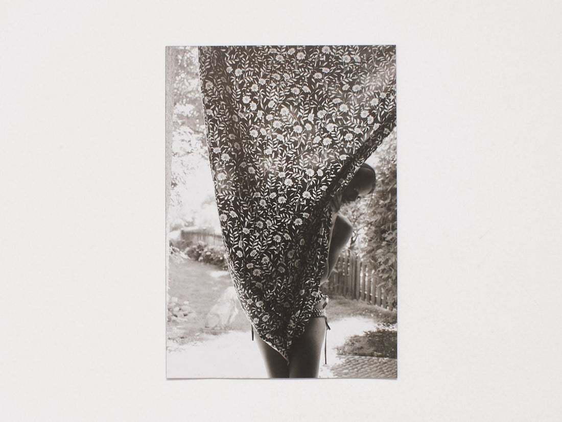 Black and white photograph of a person partially hidden behind a floral patterned fabric.